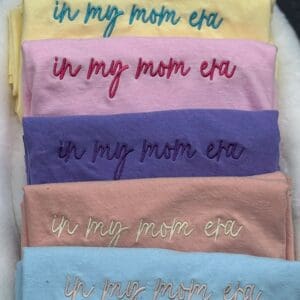 A bunch of different colored shirts with the words in mom era written on them.