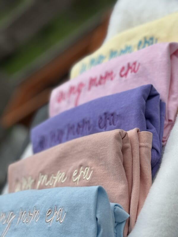 A row of folded shirts with the words " mom " written on them.